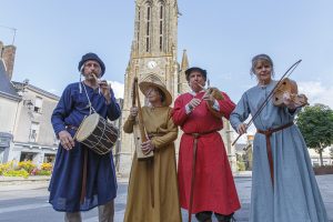 4 musiciens habillés en tenue moyenâgeuse devant la basilique, rue Notre Dame, durant la fête des 900 ans du marché de la Guerche-de-Bretagne. Samedi 4 septembre 2021.