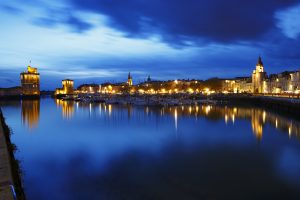 The city of La Rochelle in France, during the blue hour, view of the port with the towers of the entrance to the marina. Buildings, restaurants and hotels with illuminated facades. November 2022.