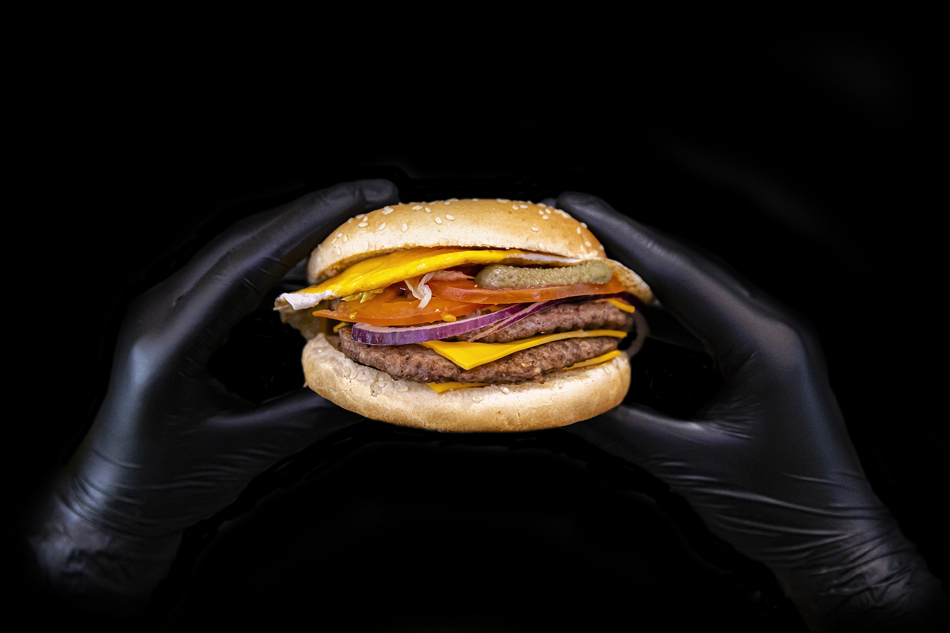 Mains de cuisinier avec gants en latex noirs qui tient un burger au milieu.