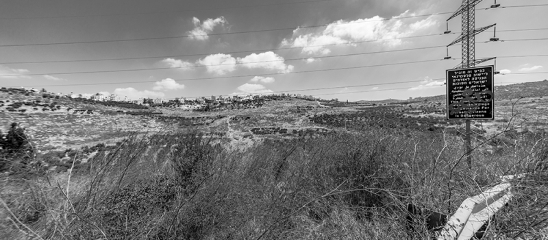 PALESTINE, august 10, 2019: Hill in Palestine with small town in the distance, Israeli sign and electric pylon, black and white picture. Palestine.